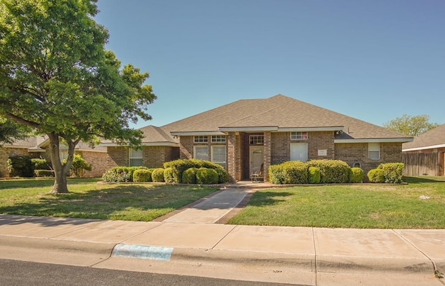 view of front facade with a shingled roof, fence, a front lawn, and brick siding