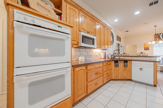 kitchen featuring a peninsula, white appliances, a sink, visible vents, and crown molding