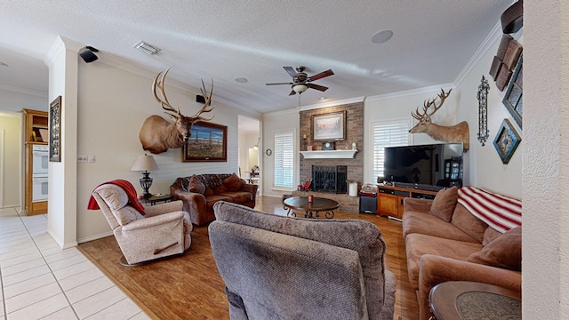 living room featuring a textured ceiling, light wood-style flooring, a large fireplace, visible vents, and ornamental molding