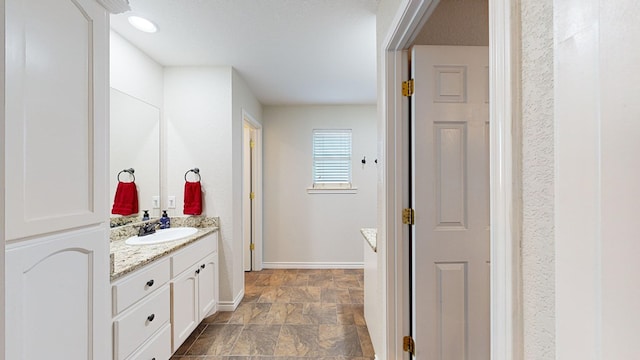 bathroom featuring stone finish flooring, baseboards, and vanity