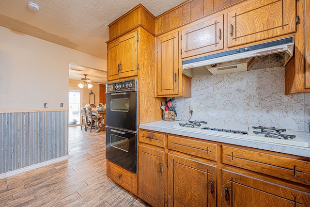 kitchen featuring light hardwood / wood-style flooring, double oven, a textured ceiling, decorative backsplash, and white gas cooktop