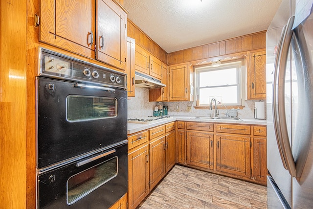 kitchen featuring sink, stainless steel refrigerator, multiple ovens, a textured ceiling, and white gas cooktop