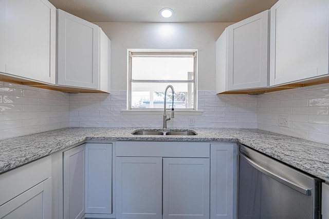 kitchen featuring light stone counters, stainless steel dishwasher, sink, and white cabinets