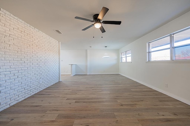 unfurnished room with hardwood / wood-style flooring, ceiling fan, and brick wall