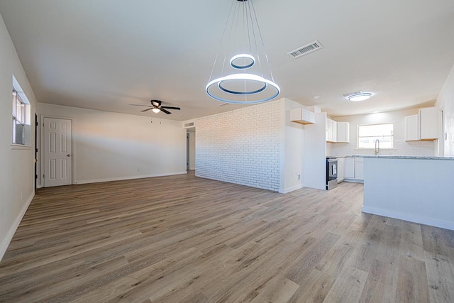 unfurnished living room featuring ceiling fan, brick wall, sink, and light hardwood / wood-style flooring