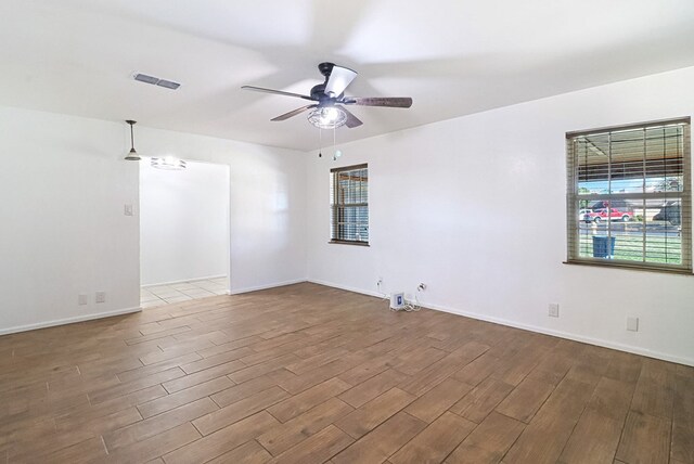 unfurnished room with baseboards, wood finished floors, visible vents, and ceiling fan