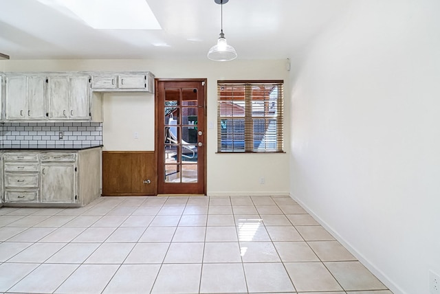 kitchen with dark countertops, backsplash, baseboards, decorative light fixtures, and light tile patterned floors