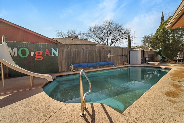 view of pool featuring a fenced in pool, a water slide, a shed, a fenced backyard, and an outbuilding