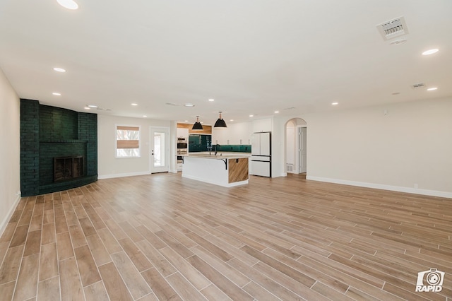 unfurnished living room with baseboards, a brick fireplace, light wood finished floors, and arched walkways