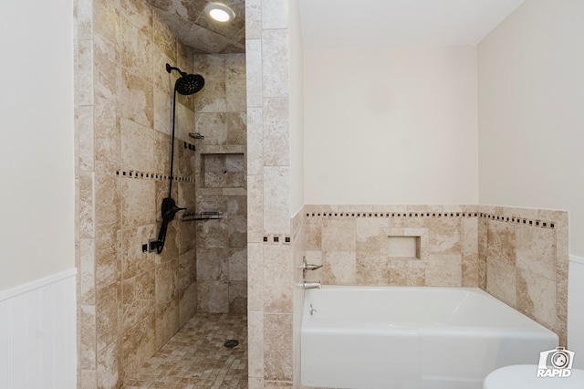 bathroom with a wainscoted wall, a garden tub, and tiled shower