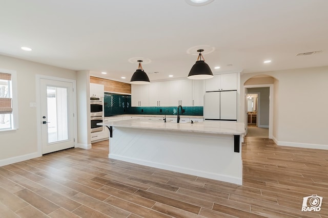 kitchen with stainless steel double oven, arched walkways, freestanding refrigerator, backsplash, and visible vents