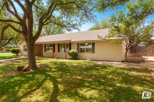 ranch-style home with brick siding, fence, a shingled roof, and a front lawn