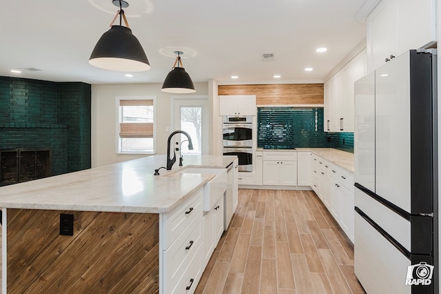 kitchen featuring freestanding refrigerator, a brick fireplace, light wood-style floors, stainless steel double oven, and a sink
