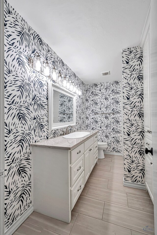 2008 Bedford Dr, Midland, TX 79701 - bathroom with wallpapered walls, toilet, vanity, and an accent wall