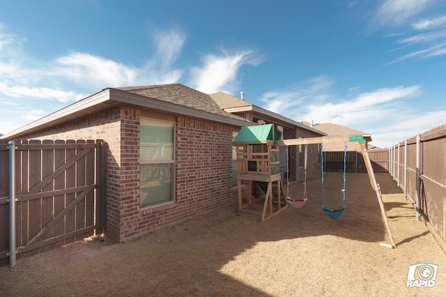 view of side of property featuring a fenced backyard, a shingled roof, a playground, and brick siding