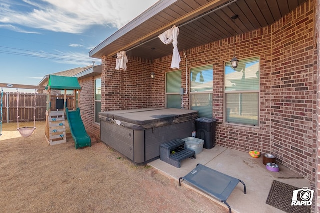 view of patio / terrace featuring a playground, fence, and a hot tub