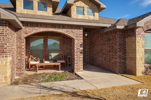 doorway to property with a shingled roof and brick siding