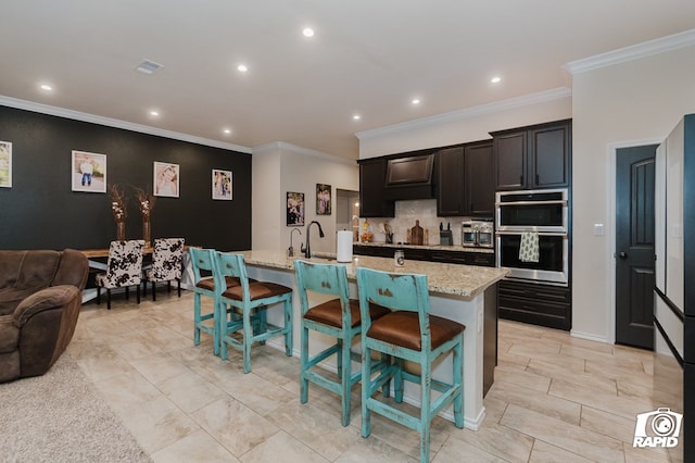 kitchen with a center island with sink, a breakfast bar area, visible vents, double oven, and open floor plan