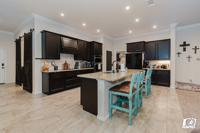 kitchen featuring visible vents, a barn door, a sink, light stone countertops, and premium range hood