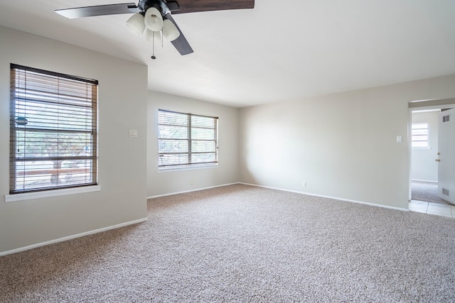 carpeted spare room with healthy amount of natural light, a ceiling fan, and baseboards