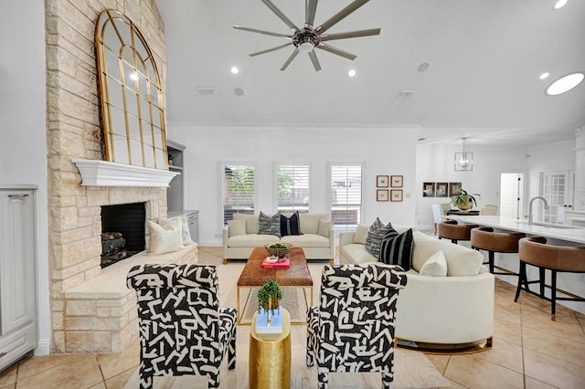 living room featuring ornamental molding, ceiling fan with notable chandelier, sink, a stone fireplace, and light tile patterned flooring