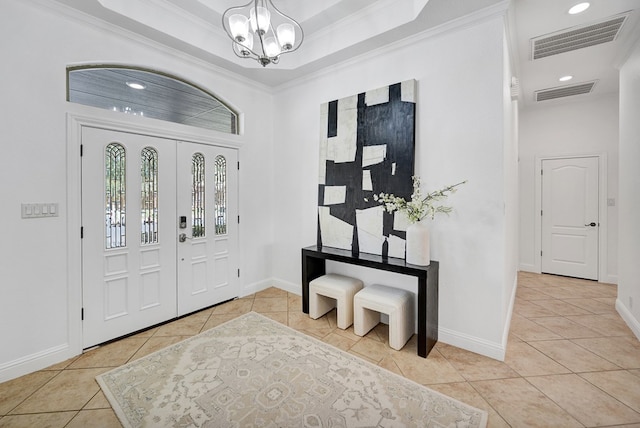 tiled foyer featuring a raised ceiling, crown molding, and a chandelier