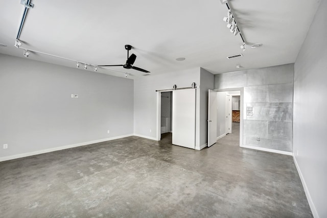 unfurnished bedroom with a barn door, rail lighting, visible vents, baseboards, and finished concrete flooring