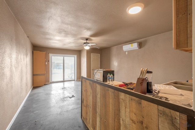 kitchen with baseboards, concrete floors, an AC wall unit, a textured ceiling, and a textured wall