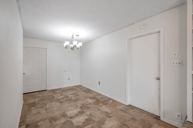 unfurnished room with a notable chandelier, a textured ceiling, and baseboards