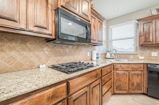 kitchen with light tile patterned flooring, light stone countertops, sink, and black appliances