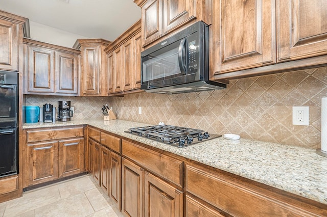 kitchen featuring tasteful backsplash, light stone counters, and black appliances