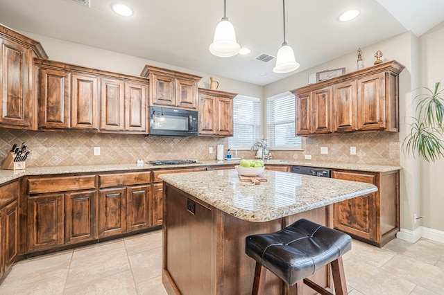 kitchen featuring decorative light fixtures, a kitchen bar, a center island, black appliances, and light stone countertops