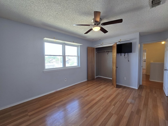 unfurnished bedroom with wood finished floors, a textured ceiling, a closet, baseboards, and ceiling fan
