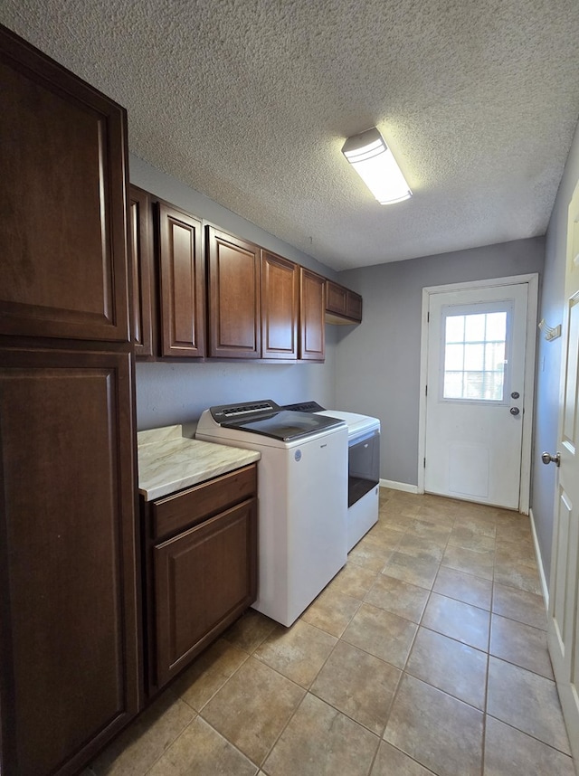 washroom with cabinet space, washer and dryer, a textured ceiling, light tile patterned flooring, and baseboards