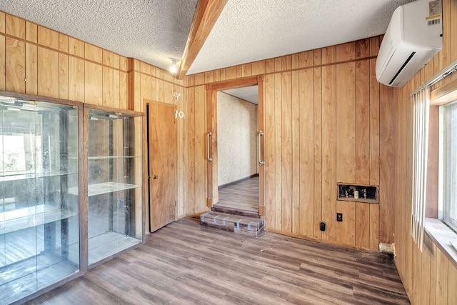 1707 Goliad St, Big Spring, TX 79720 - spare room with a wall unit AC, wood walls, wood finished floors, a textured ceiling, and healthy amount of natural light