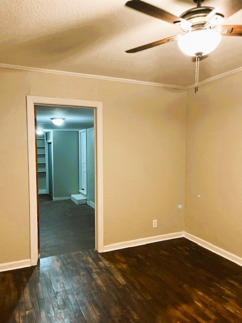 empty room featuring a ceiling fan, dark wood finished floors, and crown molding