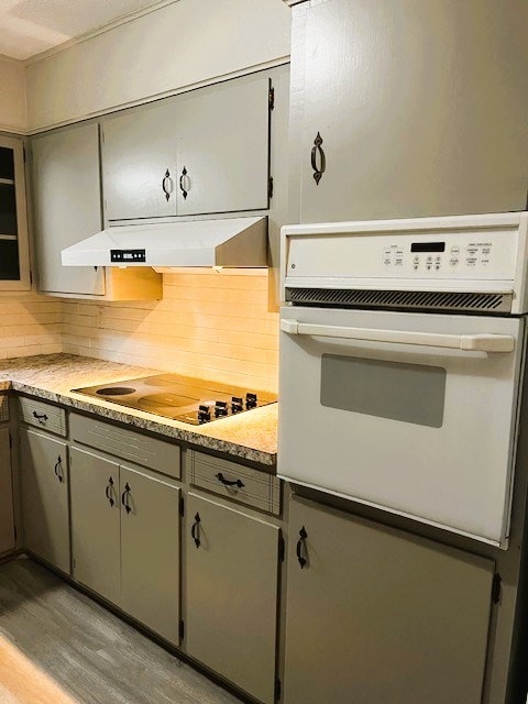 kitchen with tasteful backsplash, electric stovetop, white oven, light countertops, and under cabinet range hood