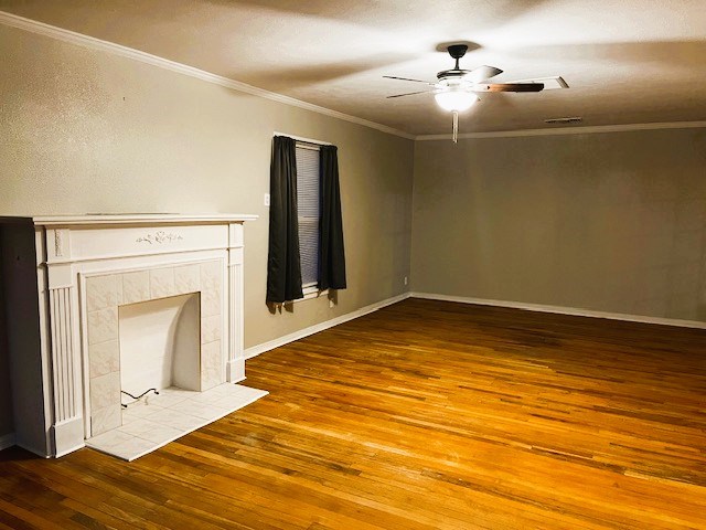 unfurnished living room with a tile fireplace, wood finished floors, a ceiling fan, baseboards, and crown molding