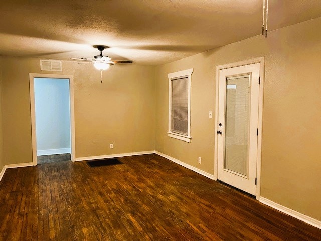 spare room with baseboards, visible vents, a ceiling fan, dark wood-type flooring, and a textured ceiling