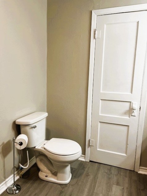 half bathroom with baseboards, toilet, and wood finished floors