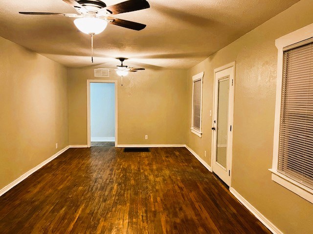 unfurnished room with dark wood-style floors, visible vents, ceiling fan, and baseboards