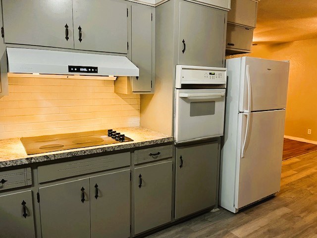 kitchen featuring tasteful backsplash, light countertops, wood finished floors, white appliances, and under cabinet range hood