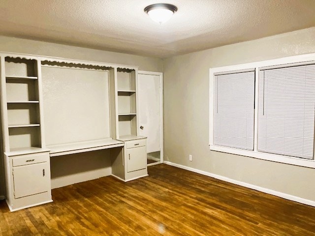 unfurnished bedroom with a textured ceiling, baseboards, dark wood-style flooring, and built in desk