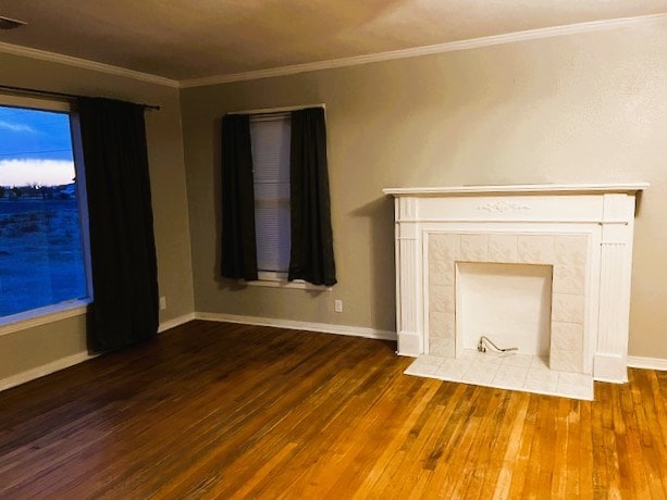 unfurnished living room with ornamental molding, a fireplace, wood finished floors, and baseboards