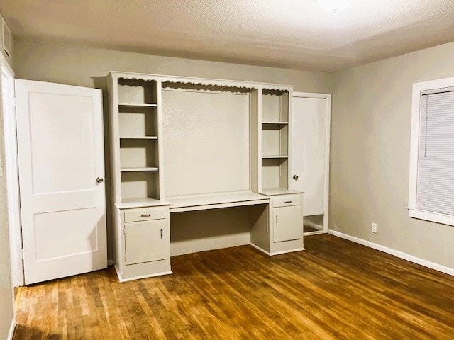 unfurnished bedroom with a textured ceiling, baseboards, dark wood-style flooring, and built in study area