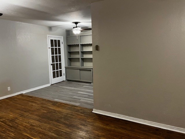 unfurnished room with dark wood-style floors, ceiling fan, a textured ceiling, and baseboards