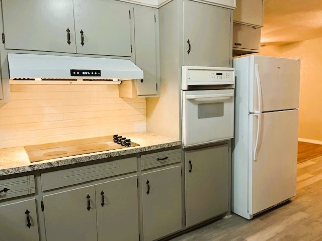 kitchen featuring white appliances, decorative backsplash, light countertops, light wood-type flooring, and under cabinet range hood