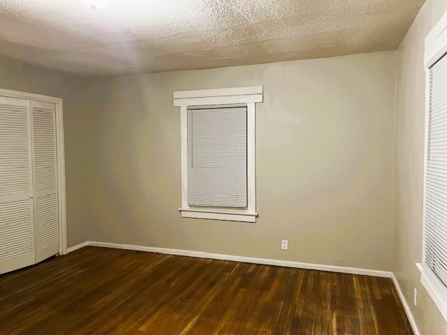 unfurnished bedroom with dark wood-style floors, a closet, a textured ceiling, and baseboards