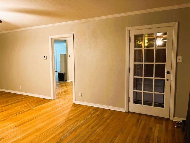 spare room with baseboards, wood-type flooring, and crown molding