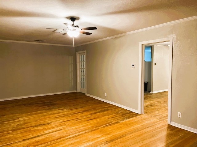 empty room with visible vents, ornamental molding, a ceiling fan, wood finished floors, and baseboards